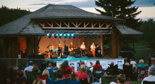 a band on an outdoor stage at dusk, on the banks of the Athabasca river
