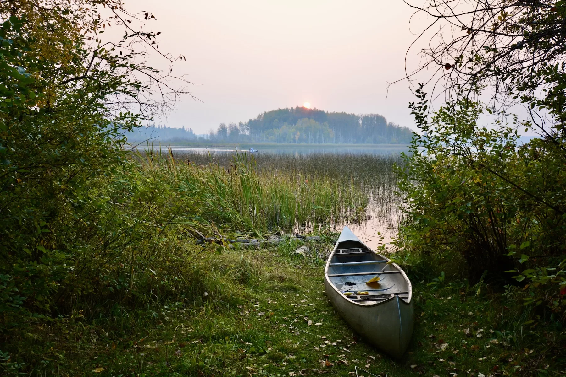 a canoe on the shore of Island Lake with the sun setting behind a tree covered island